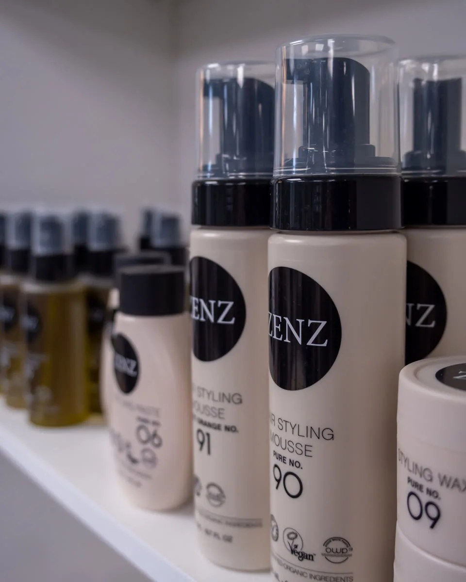 Rij crèmekleurige Zenz-stylingproducten op een salonschap.